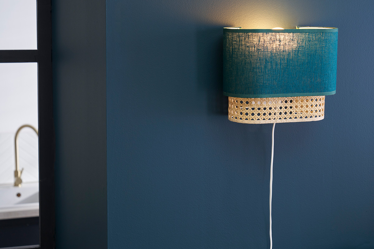 Applique da parete blu pavone e rattan, vista laterale, su muro blu.