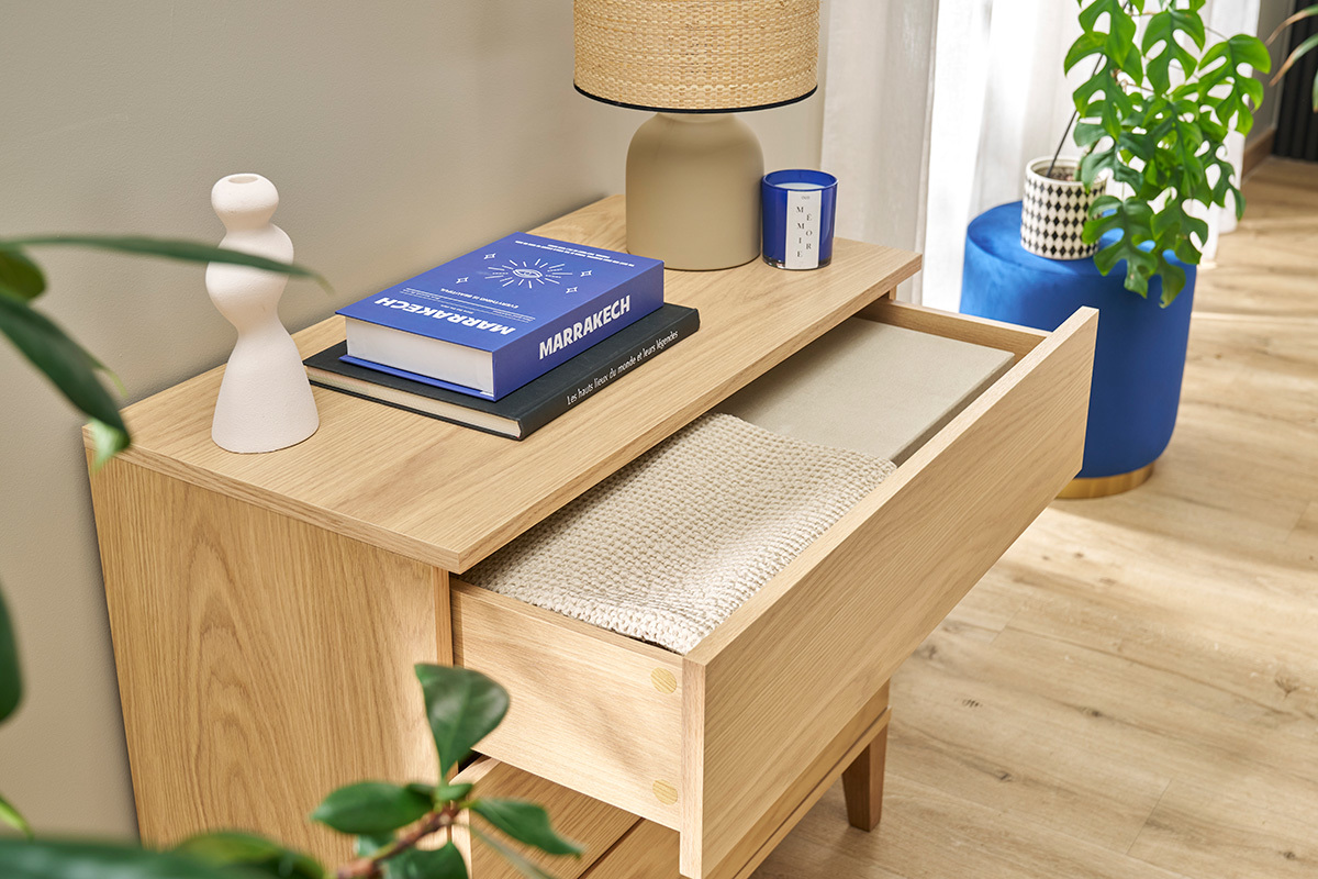 Comodino scandinavo in legno chiaro con un cassetto aperto, vista dall'alto, con una lampada e libri sopra.