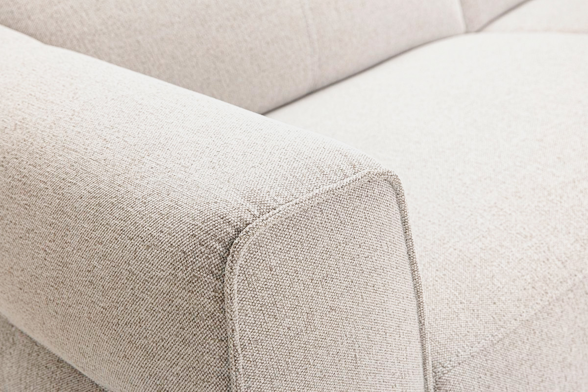 Dettaglio del divano a 3 posti in tessuto beige, che mette in evidenza il poggiatesta e il bracciolo quadrato.