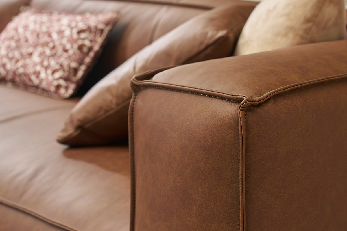 Bracciolo del divano ad angolo in pelle marrone con cuscini.