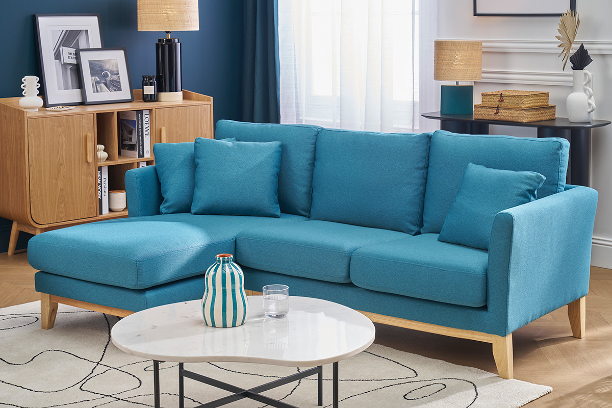 Divano ad angolo sinistro blu petrolio e legno chiaro, in un salotto con tavolino e buffet in legno.