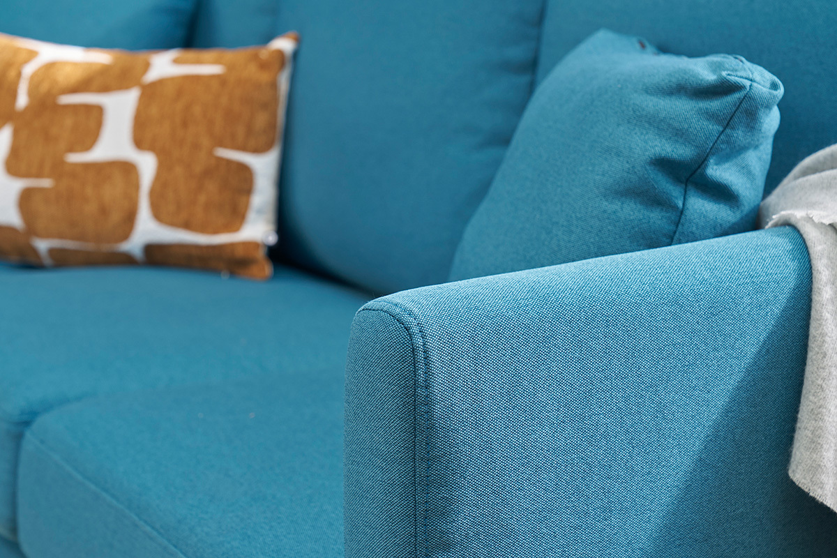 Primo piano su un divano ad angolo blu petrolio con cuscini.