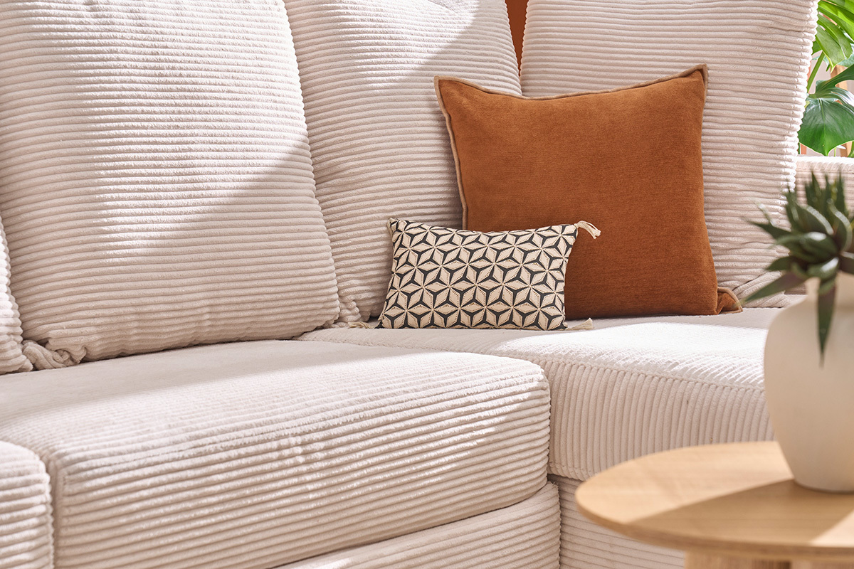 Divano ad angolo beige in velluto a coste con cuscini decorativi visti di lato.