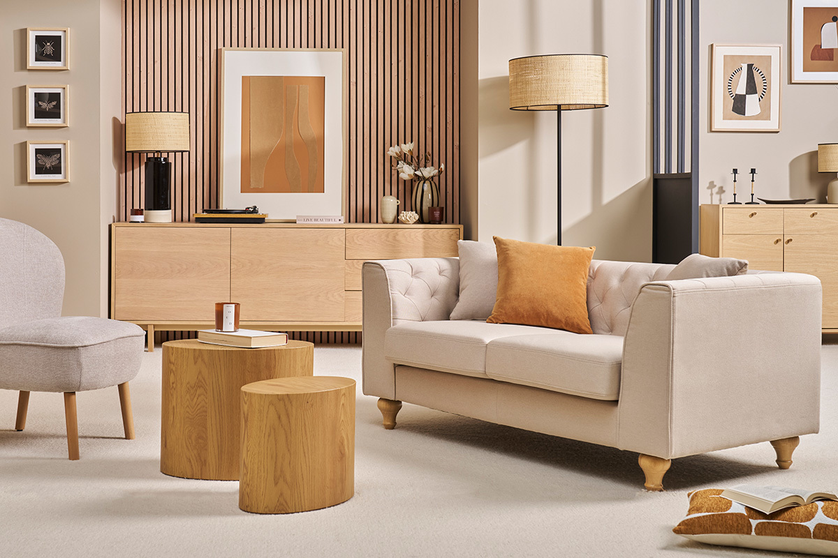 Divano a 2 posti capitonn beige MONTAIGNE in tessuto, vista laterale con cuscino arancione, in un salotto elegante.