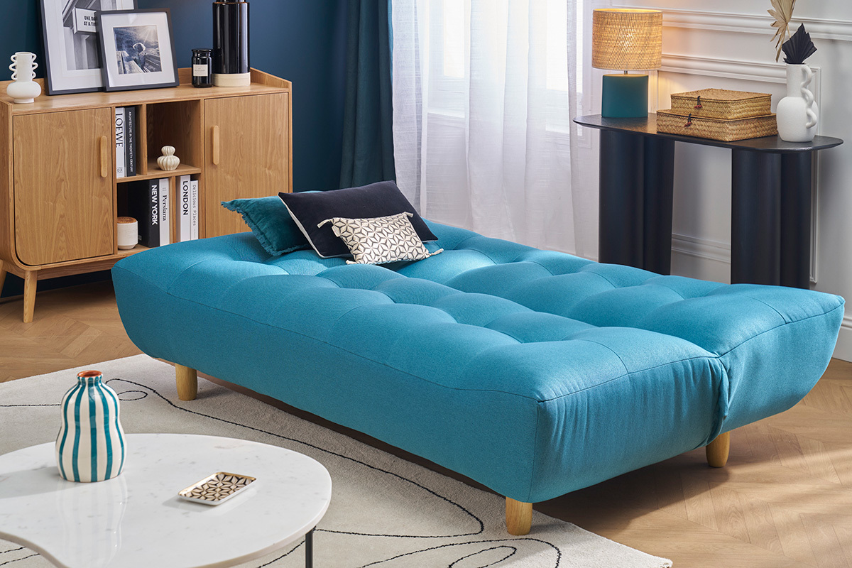 Divano letto scandinavo blu petrolio con piedi in legno, visto di lato in un soggiorno.
