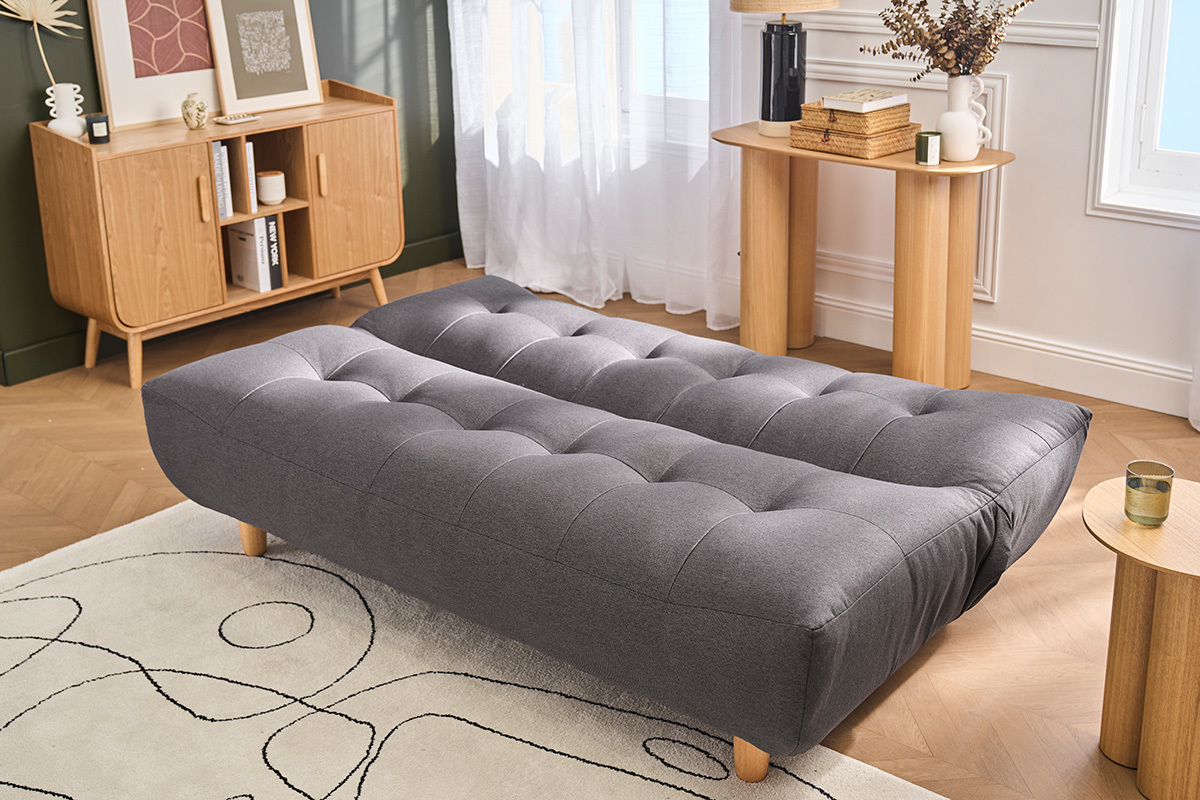Divano letto scandinavo grigio scuro YUMI aperto, con piedi in legno chiaro, in un soggiorno.
