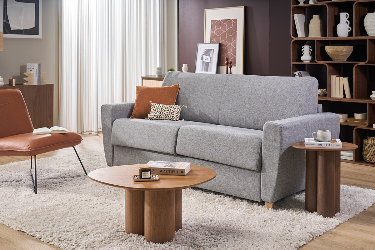 Divano letto GRAHAM in tessuto grigio chiaro con cuscini, accompagnato da tavolini bassi, vista frontale.
