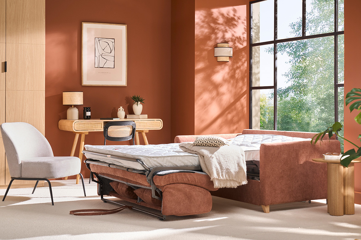 Divano letto in tessuto terra bruciata, materasso aperto, in un soggiorno con parete color terra cotta.