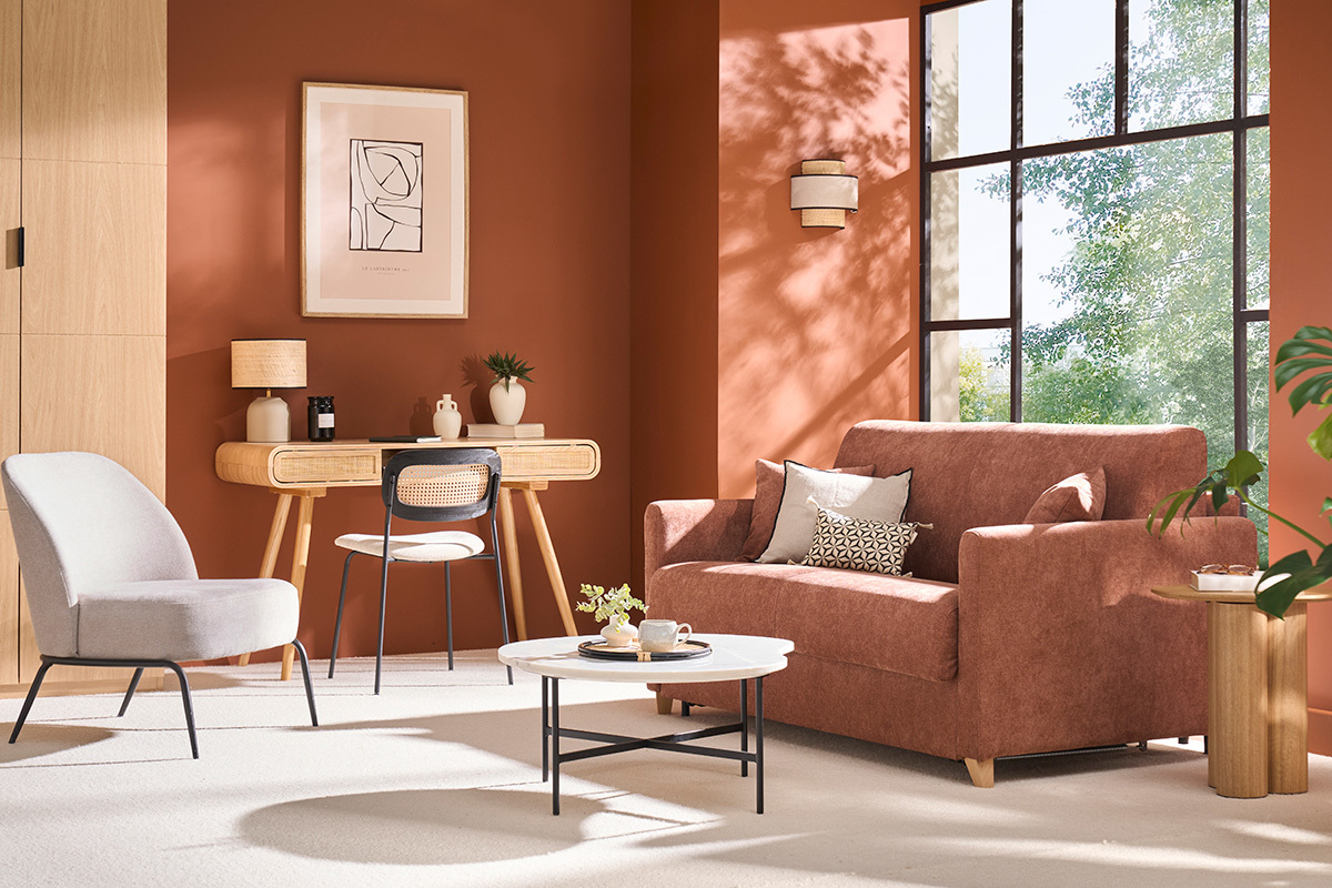 Divano letto in tessuto terra bruciata in un soggiorno con scrivania e poltrona.