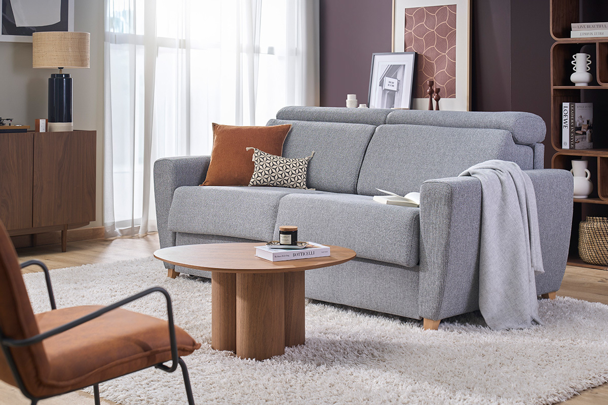 Divano letto 3 posti grigio con poggiatesta regolabili, vista a 3/4 in un soggiorno moderno