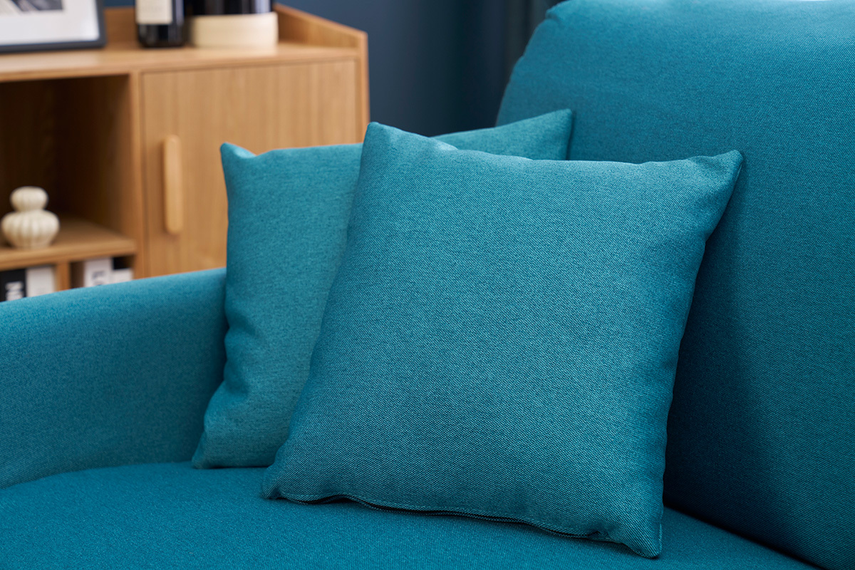 Cuscini del divano letto blu petrolio SKANDY in vista ravvicinata accanto a un mobile in legno.
