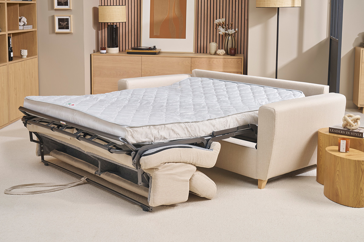 Divano letto beige con materasso aperto in un soggiorno.