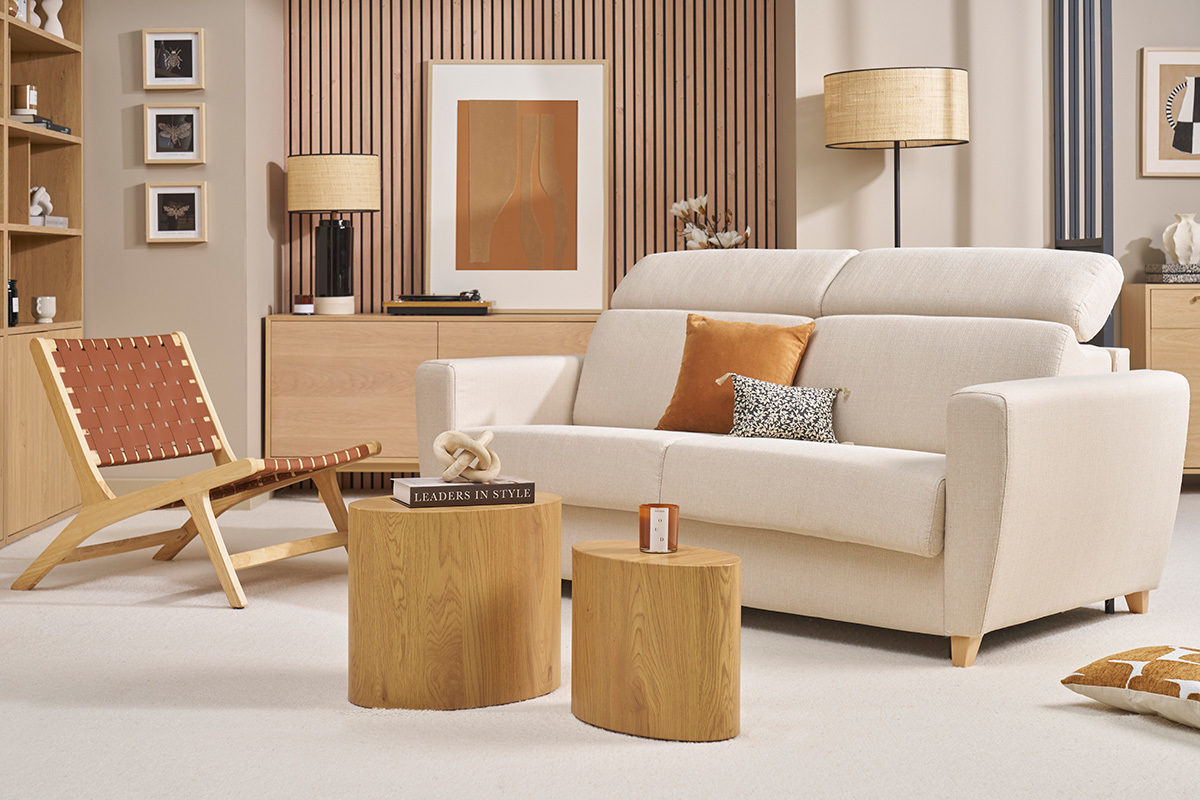 Divano letto beige GOYA con poggiatesta regolabili, vista frontale, in un soggiorno con mobili in legno chiaro.