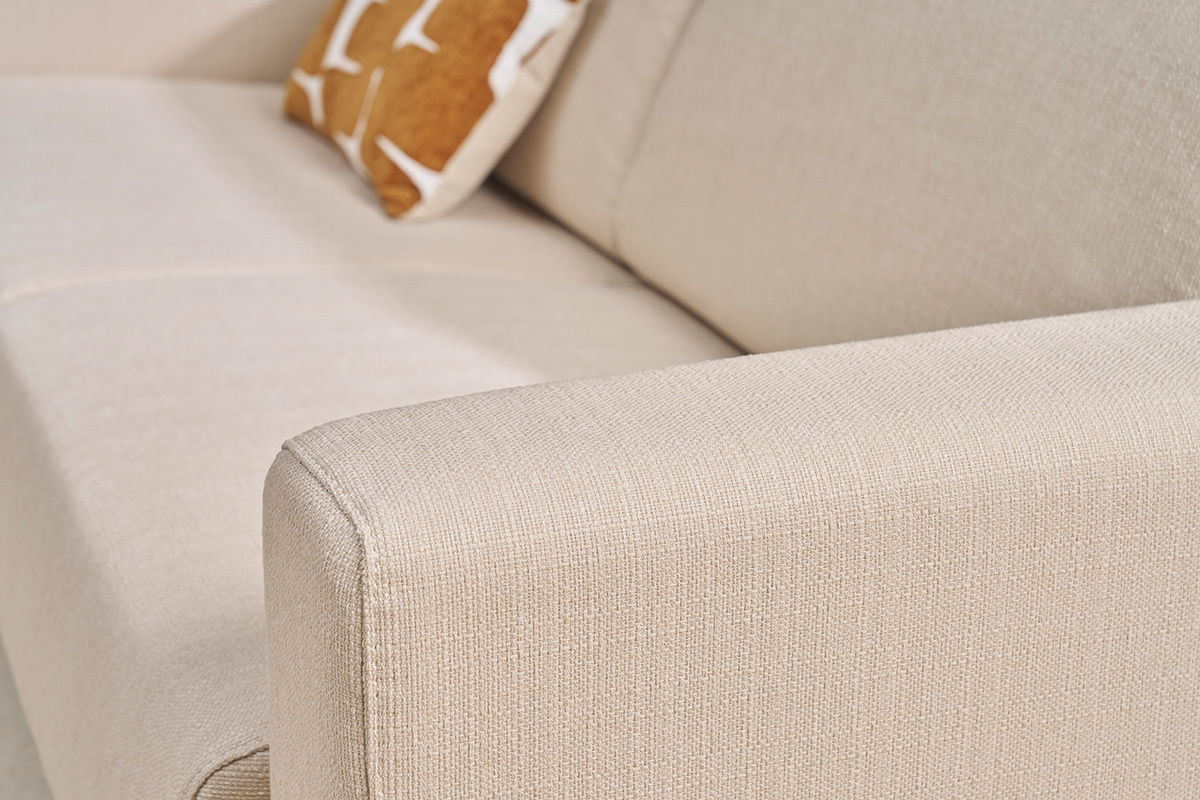 Bracciolo di un divano beige in tessuto con cuscino decorativo. Vista ravvicinata.