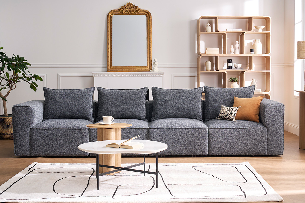 Divano modulare a 5 posti in tessuto grigio, vista frontale, con tavolino e decorazioni.