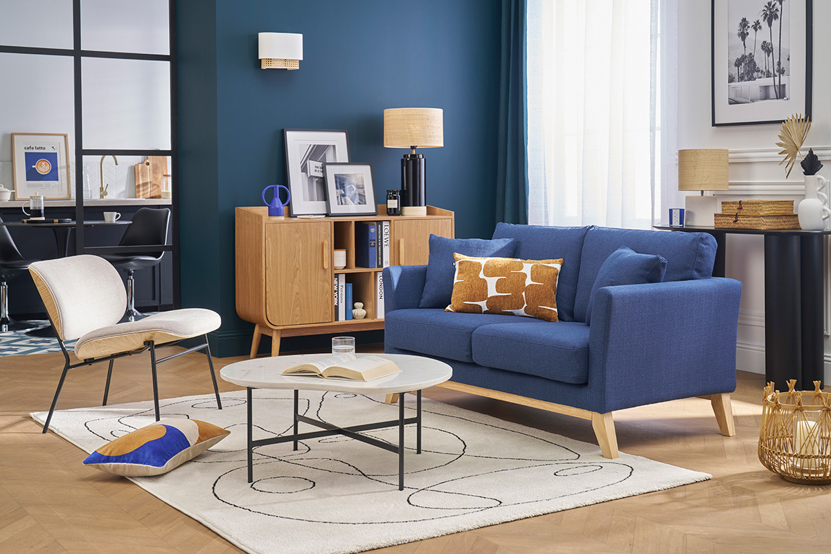 Soggiorno con divano scandinavo blu scuro in tessuto e piedi in legno, tavolino e mobile in legno chiaro.