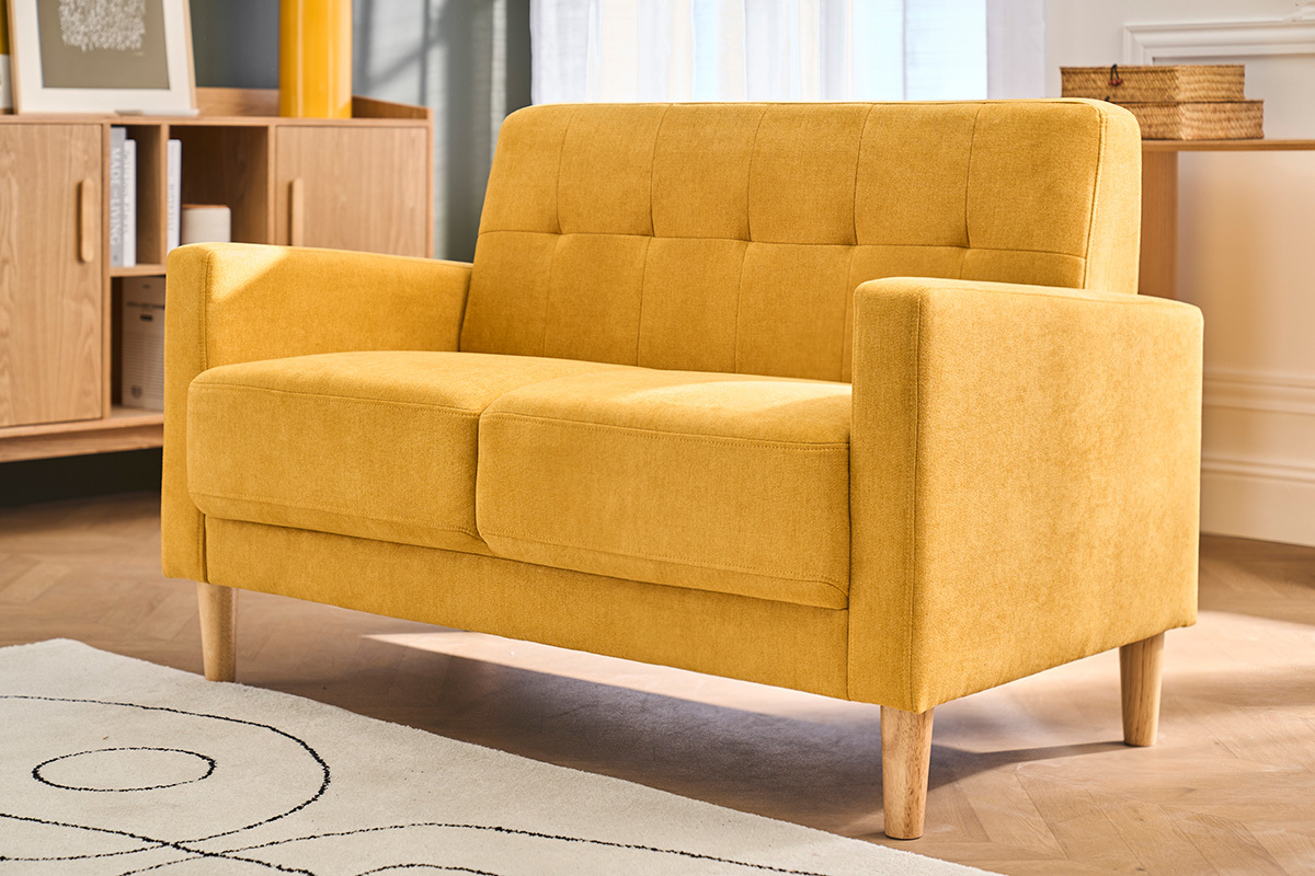 Divano scandinavo 2 posti giallo senape, piede in legno, vista angolare in un salotto moderno.