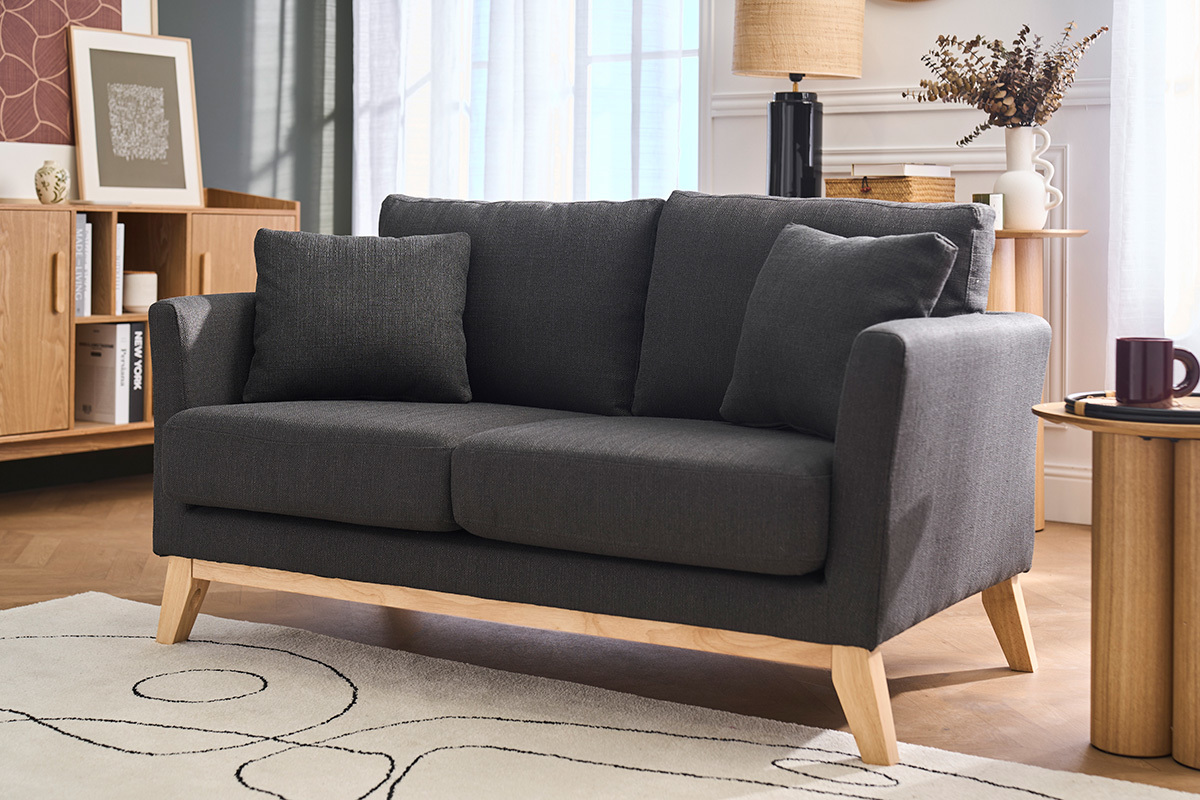 Divano a 2 posti in tessuto grigio scuro e legno chiaro, vista da 3/4 in un salotto.