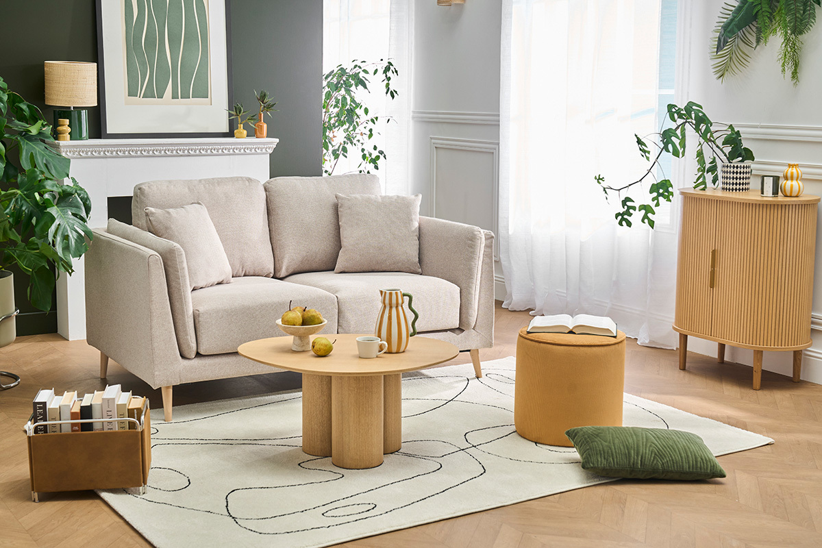 Divano scandinavo a 2 posti beige con cuscini, tavolo e accessori decorativi in un soggiorno luminoso.