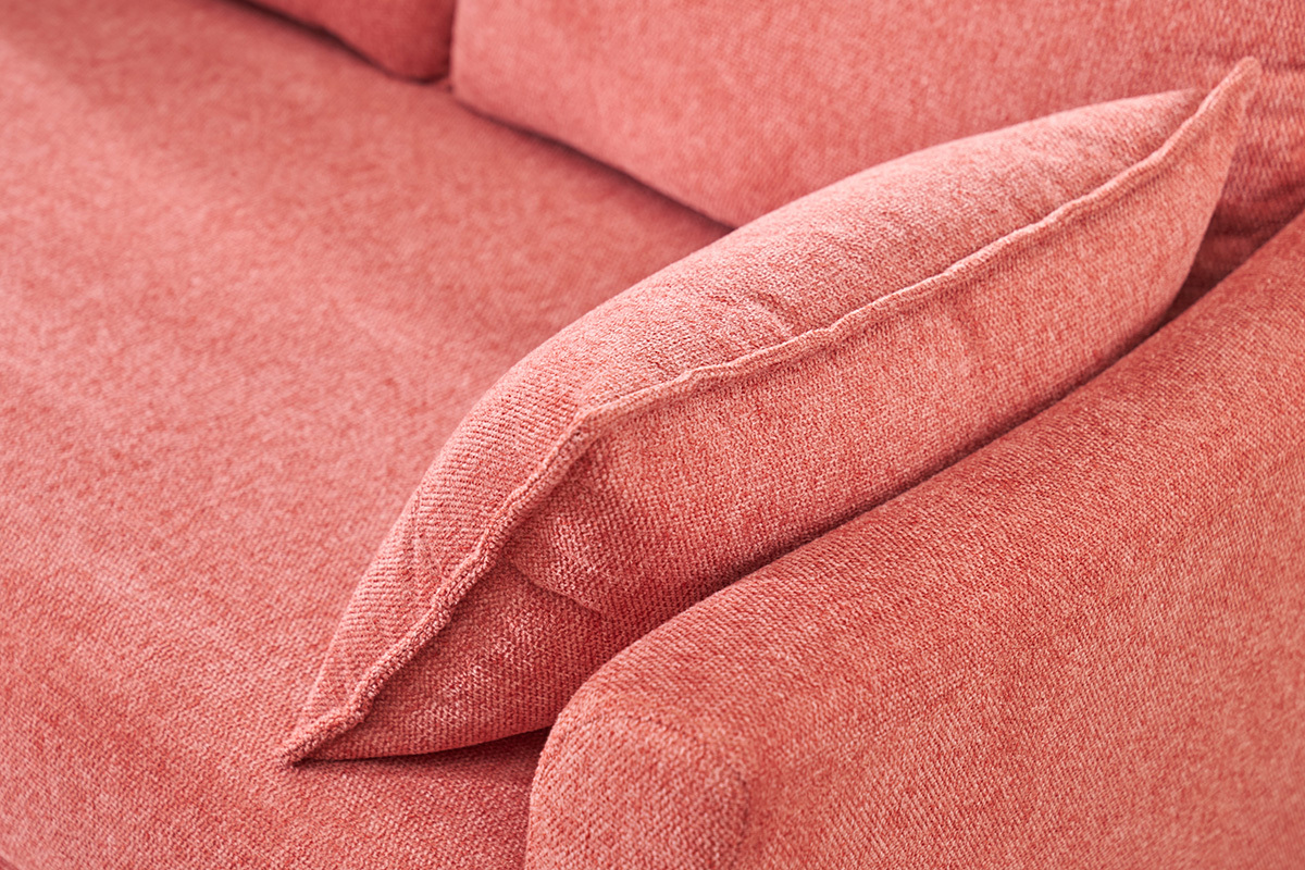 Primo piano su bracciolo e cuscino di un divano in tessuto effetto velluto terracotta.