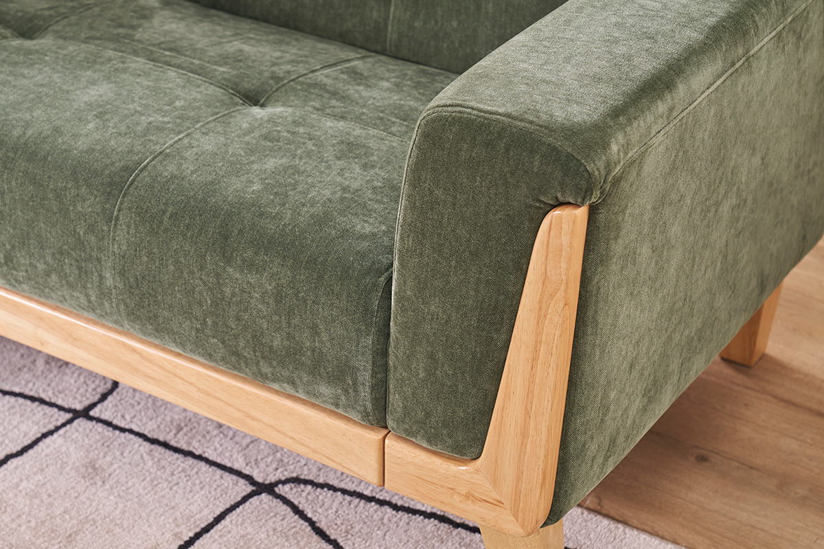 Dettaglio di un divano scandinavo verde kaki in tessuto effetto velluto con bracciolo in legno chiaro.
