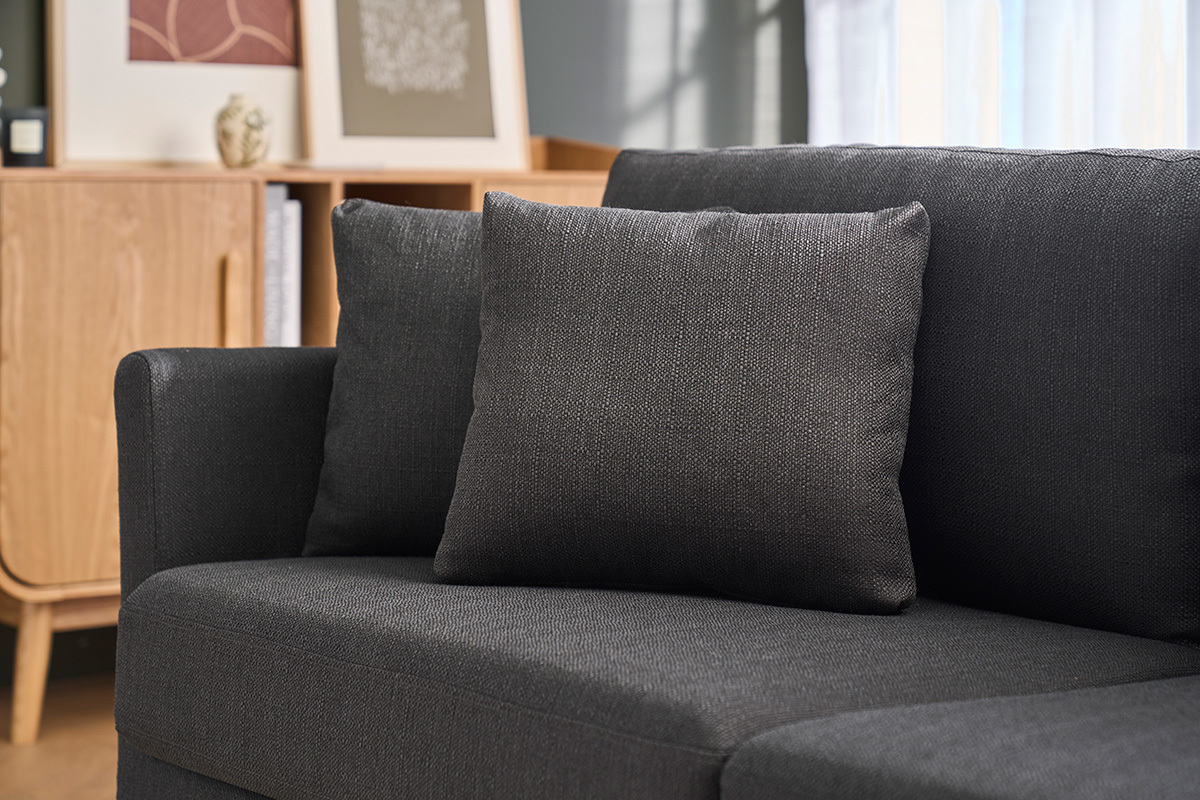 Divano scandinavo grigio scuro con cuscini, vista parziale, mobile in legno chiaro sullo sfondo.