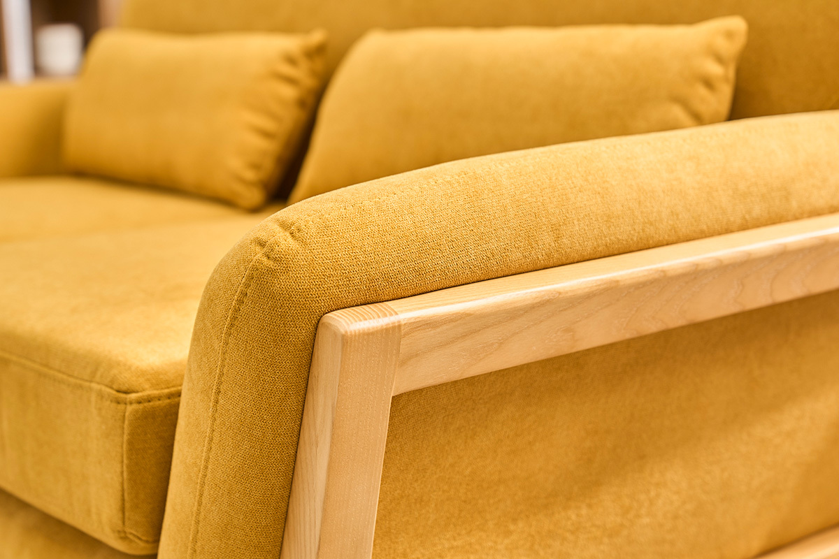 Dettaglio di un divano scandinavo a 2 posti in tessuto giallo senape con bracciolo in legno chiaro.