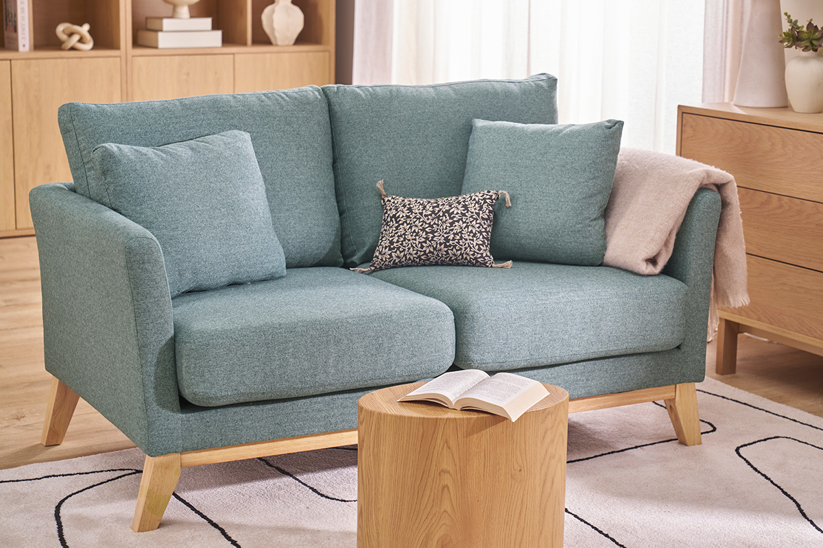 Divano scandinavo a 2 posti verde grigio con cuscini, tavolino davanti.