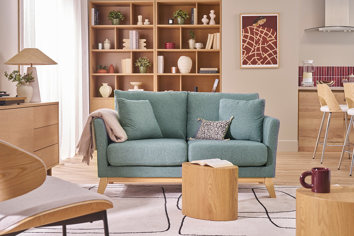 Divano a 2 posti in tessuto verde grigio e legno chiaro con cuscini, vista frontale in un soggiorno.