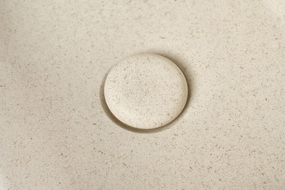 Lavabo quadrato in pietra naturale beige con scarico, vista ravvicinata, finitura opaca.