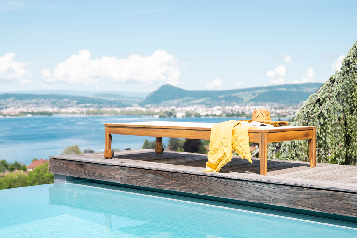 Lettini NAVEEN in legno massiccio vicino a una piscina, con un asciugamano giallo e un cappello di paglia.