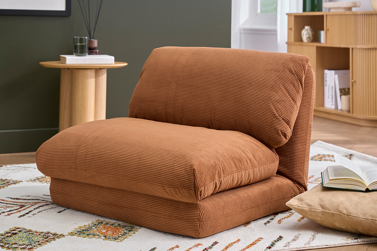 Poltrona SPENCER in velluto a coste color terra bruciata, vista da tre quarti, su un tappeto in un salotto.