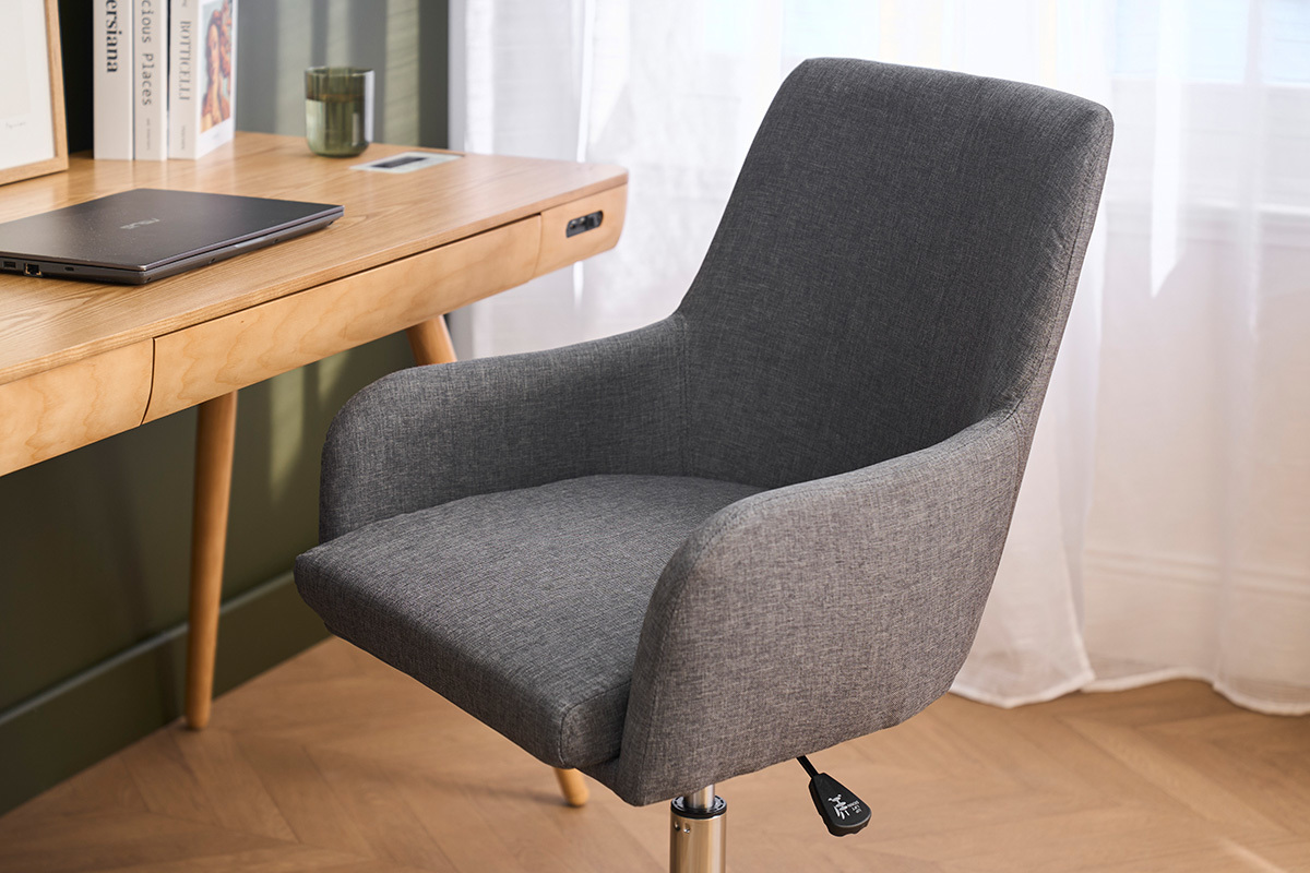 Sedia da ufficio in tessuto grigio, vista da 3/4, con braccioli davanti a una scrivania in legno.