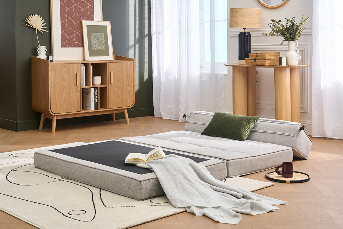 Divano letto 2 posti KATY aperto, tessuto grigio chiaro, cuscino verde, situato in un salotto moderno.