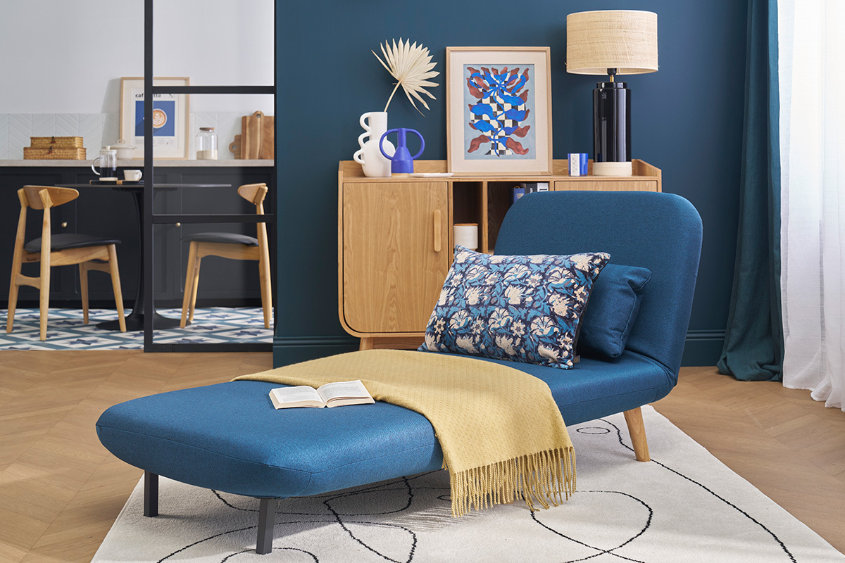 Poltrona convertibile AMIKO blu scuro su sfondo di decorazione scandinava, vista laterale.