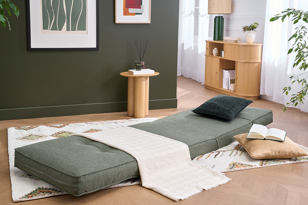 Poltrona letto SALLY convertibile in tessuto verde kaki, aperta, con cuscini e coperta su tappeto.