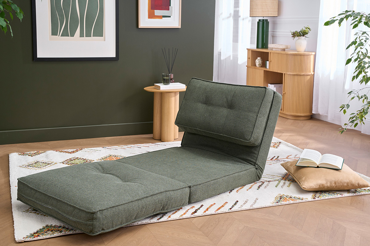 Poltrona letto convertibile in tessuto verde kaki, vista laterale, su un tappeto in un salotto luminoso.
