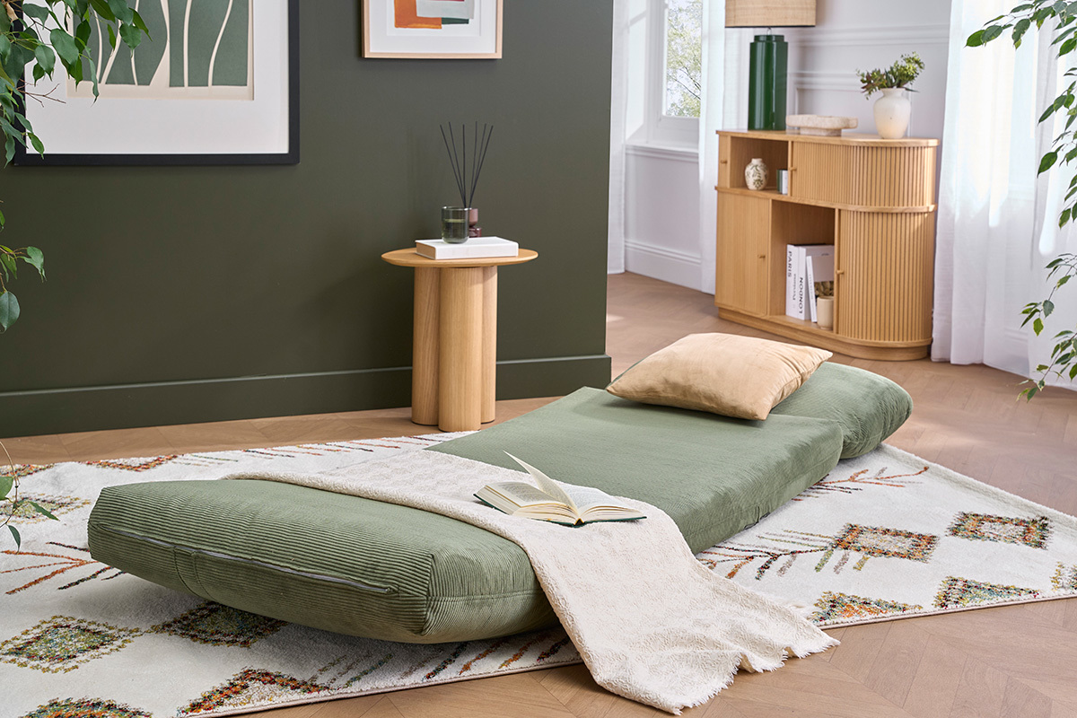 Poltrona letto SPENCER in velluto a coste verde kaki aperta su un tappeto, con cuscino beige.