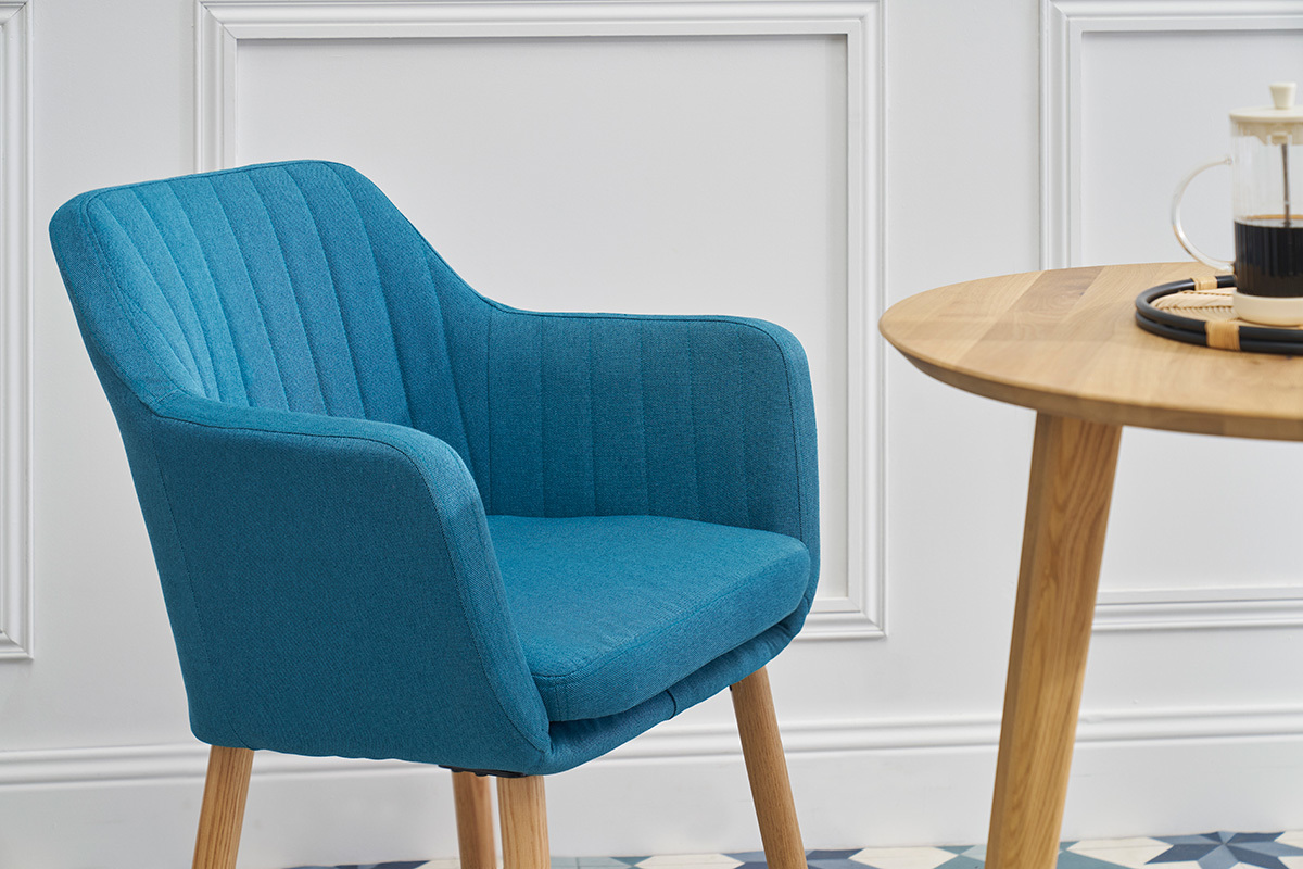 Sedia scandinava blu ALEYNA in tessuto, vista di lato, con un tavolo in legno.