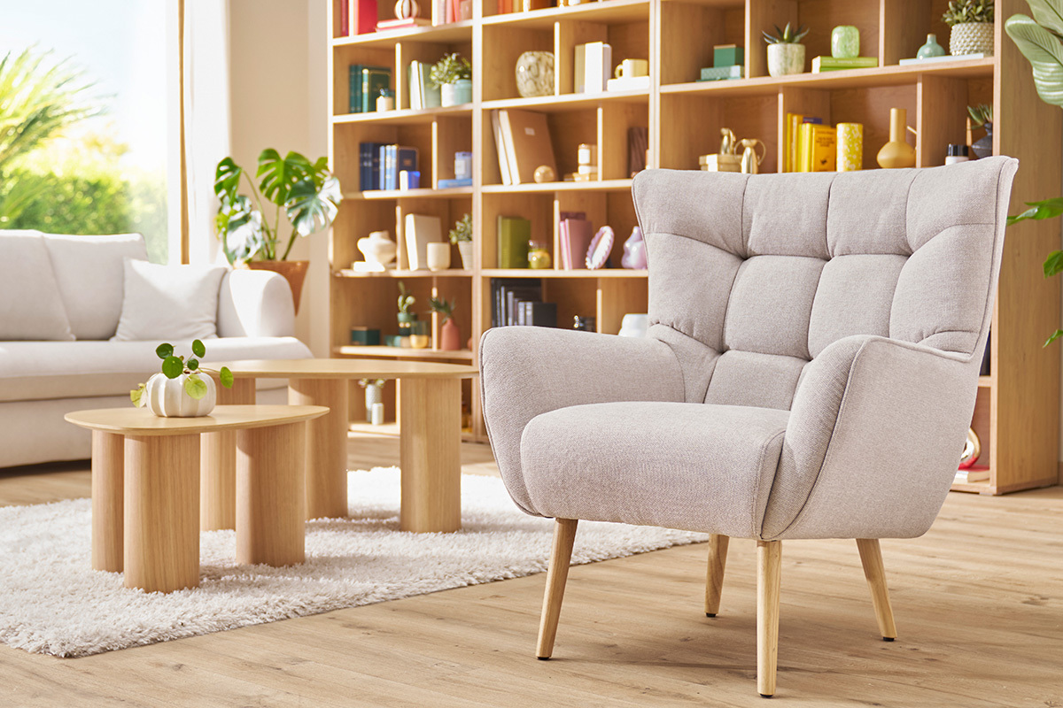 Poltrona scandinava AVERY in tessuto beige, struttura in legno, in un interno luminoso.