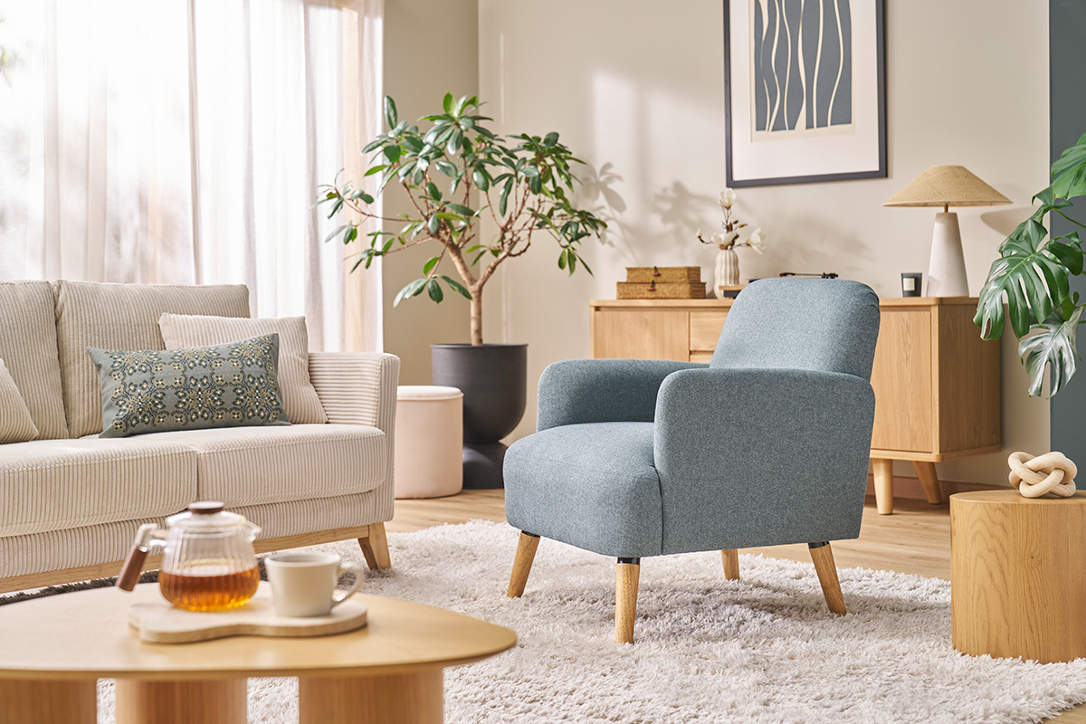 Poltrona scandinava in tessuto con piedi in legno chiaro, posizionata in un soggiorno moderno.