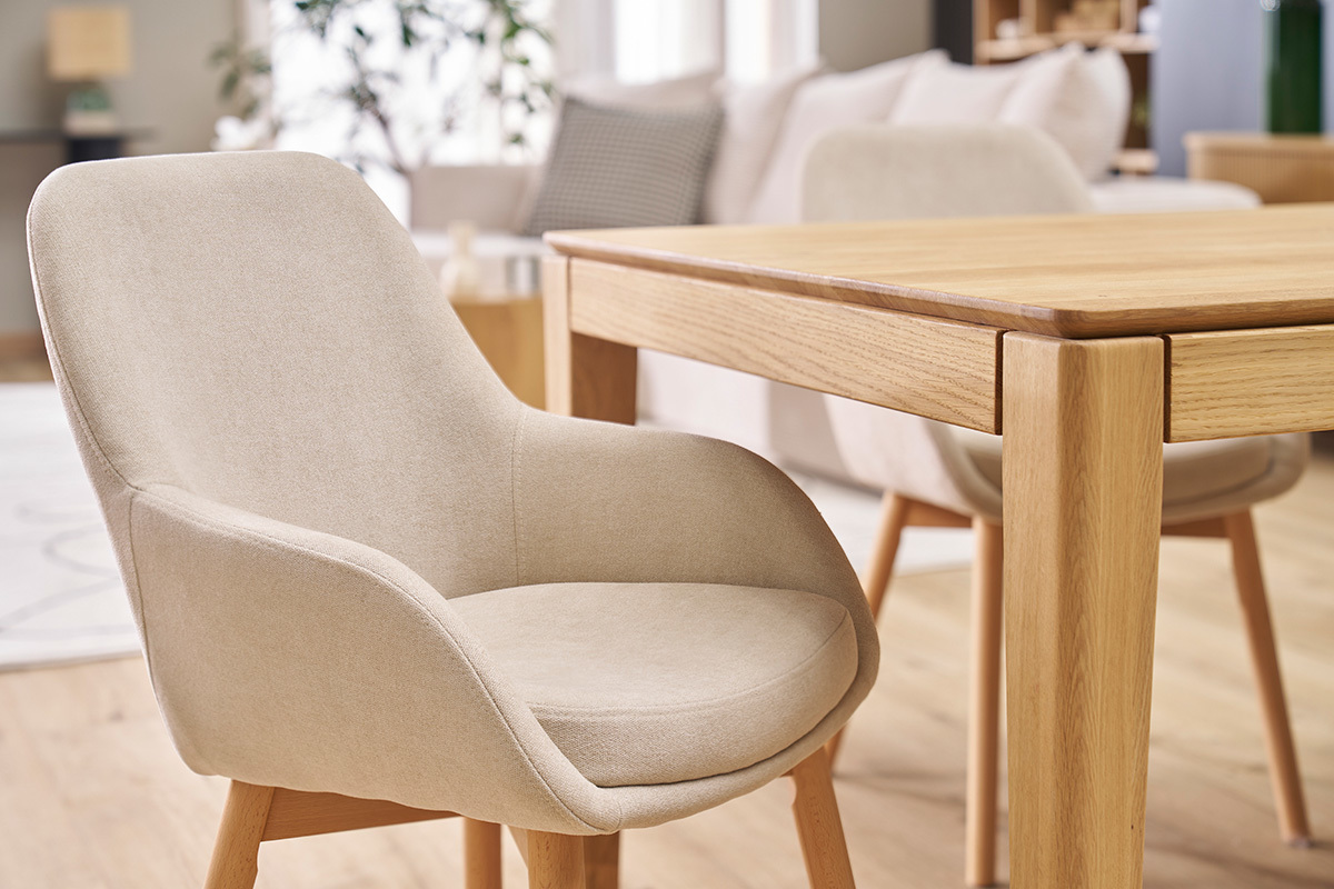 Poltrona scandinava in tessuto beige e legno chiaro, vista laterale, accanto a un tavolo in legno.
