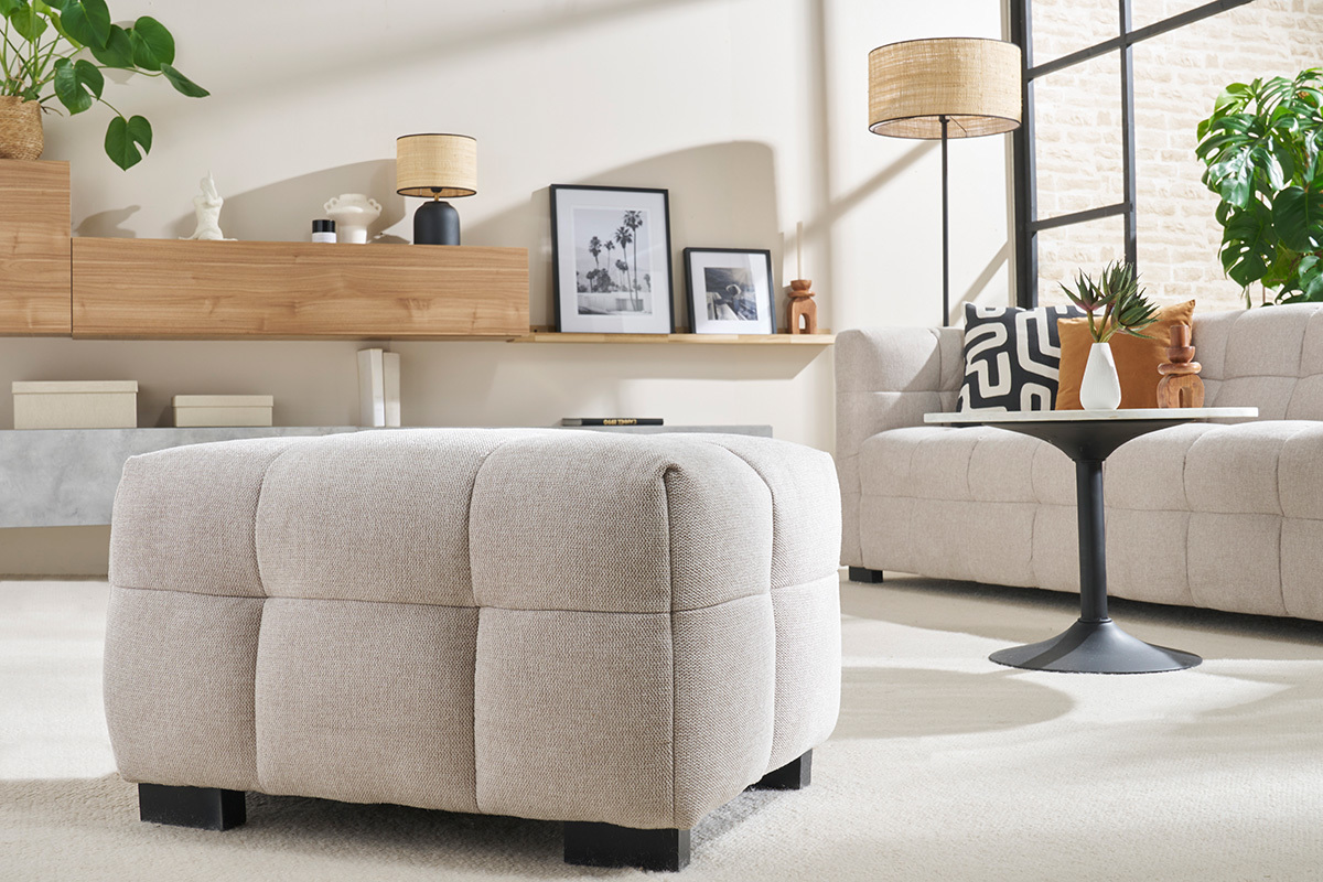 Soggiorno moderno con pouf in tessuto beige, tavolino rotondo nero e divano abbinato.