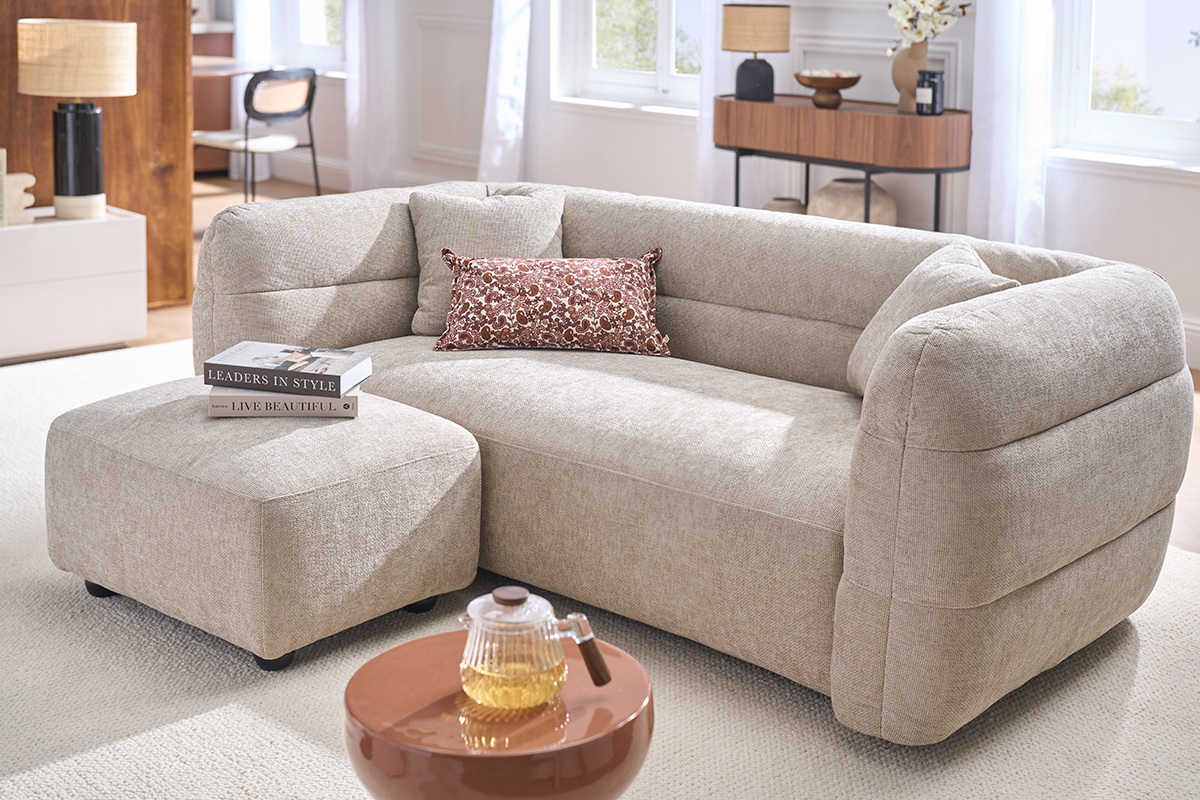 Pouf poggiapiedi in tessuto beige, in un soggiorno moderno, vicino a un divano.