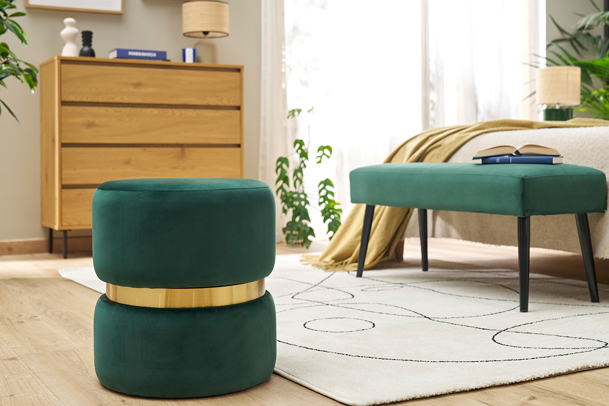 Pouf rotondo in velluto verde scuro con banda dorata, posizionato in un salotto moderno.