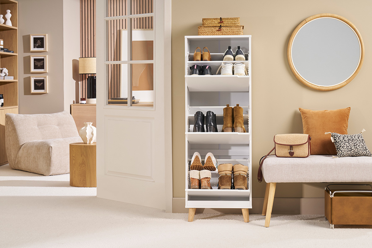 Mobile porta scarpe bianco con 3 scomparti e piedi in quercia, pieno di scarpe, in un interno moderno.