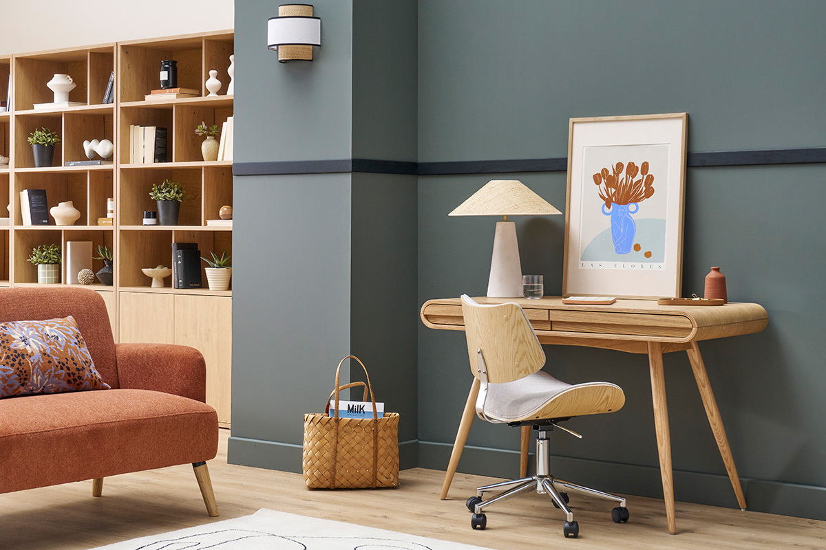 Scrivania scandinava in legno chiaro con lampada e sedia davanti a una parete grigia.