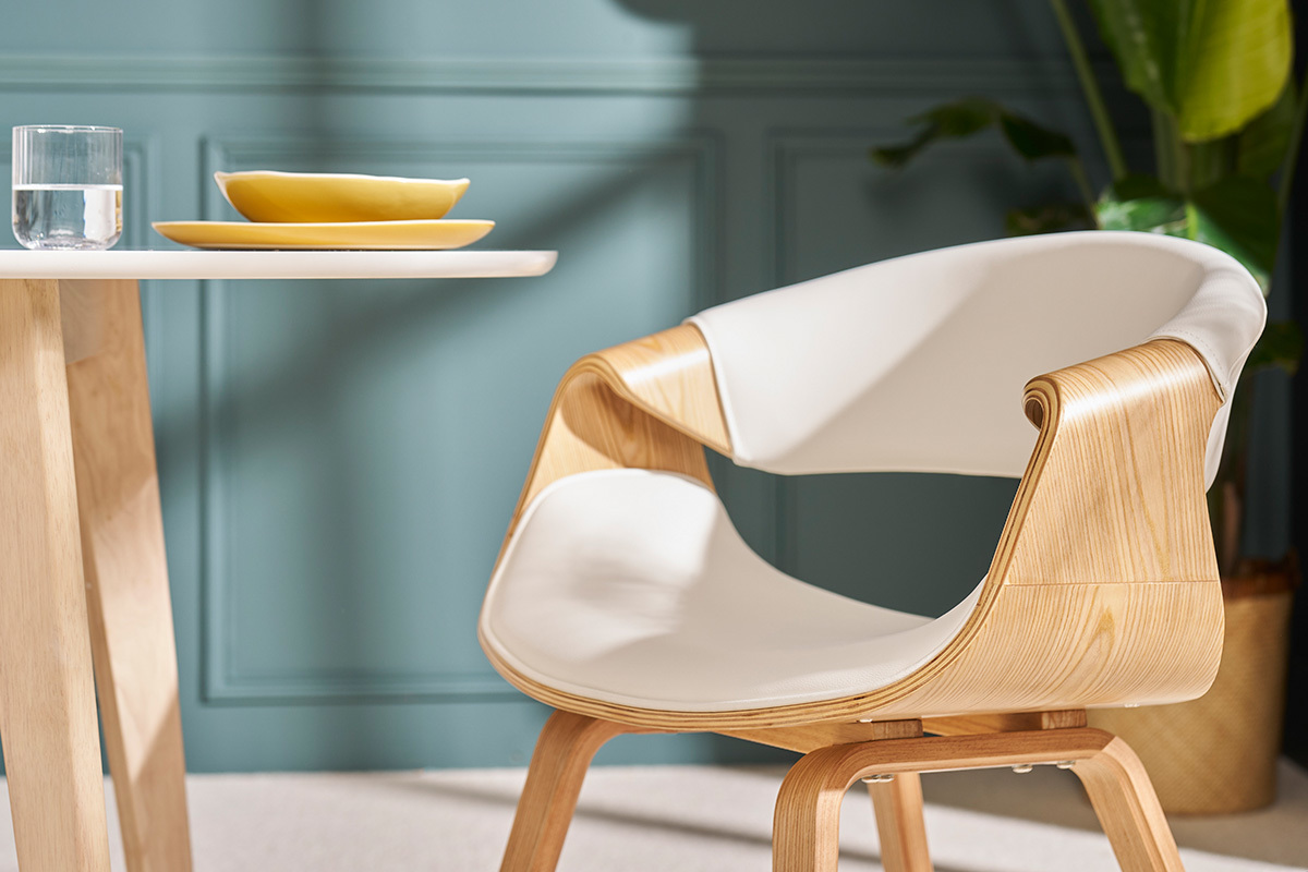 Sedia di design ARAMIS bianca con braccioli, vista laterale, accanto a un tavolo.