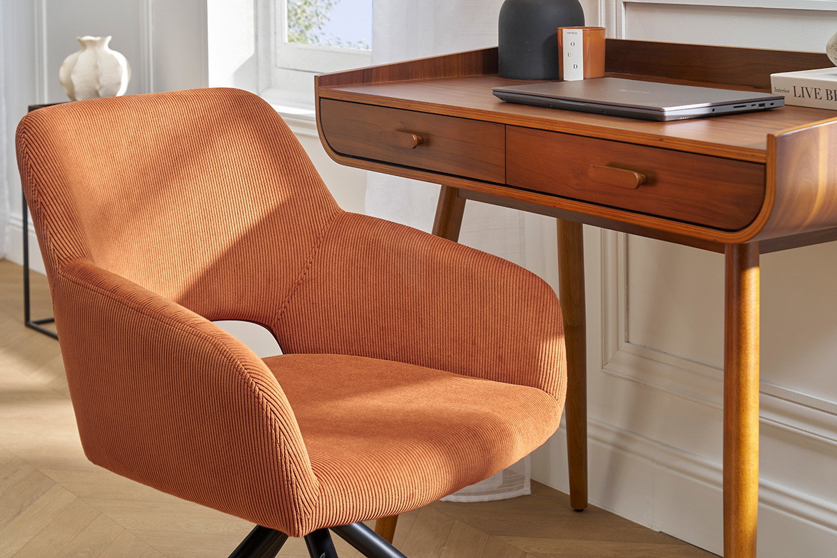 Sedia girevole in velluto a coste color terra bruciata accanto a una scrivania in legno, vista d'interno.