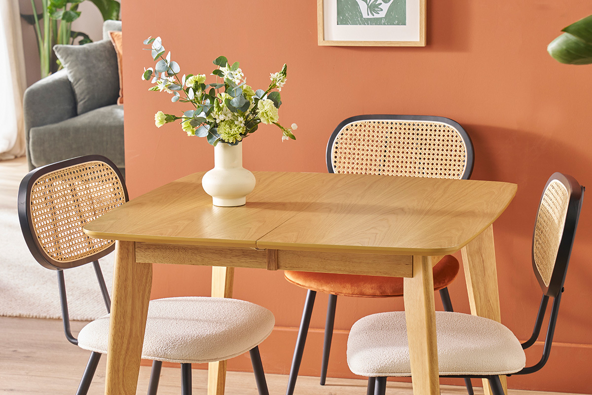 Due sedie SWANN in tessuto bianco e rattan intorno a un tavolo in legno chiaro, vaso con fiori.